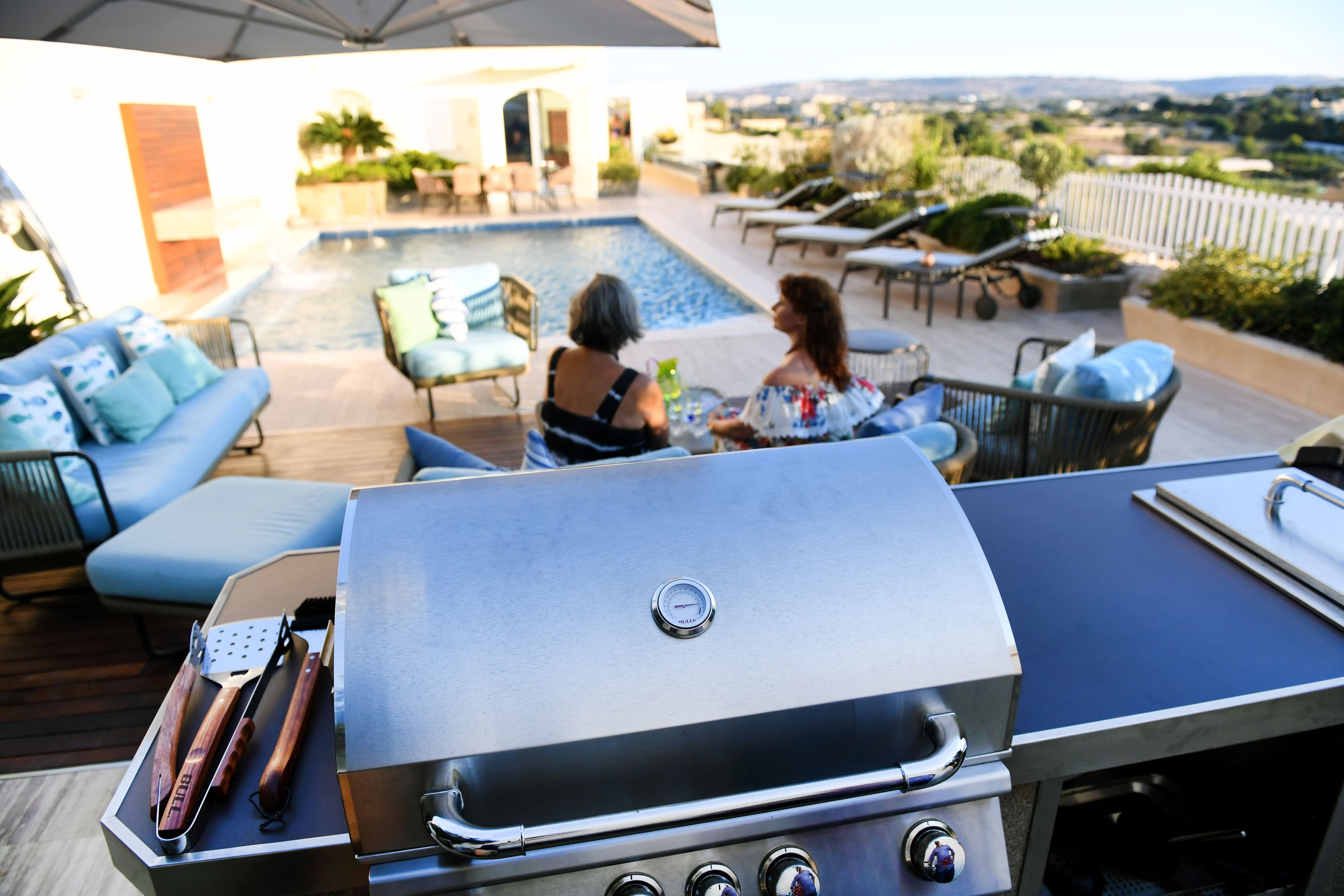 Premium gas grill with the hood open showing lit main burners, cast stainless burner tubes, and a hot grate ready for direct-heat searing.