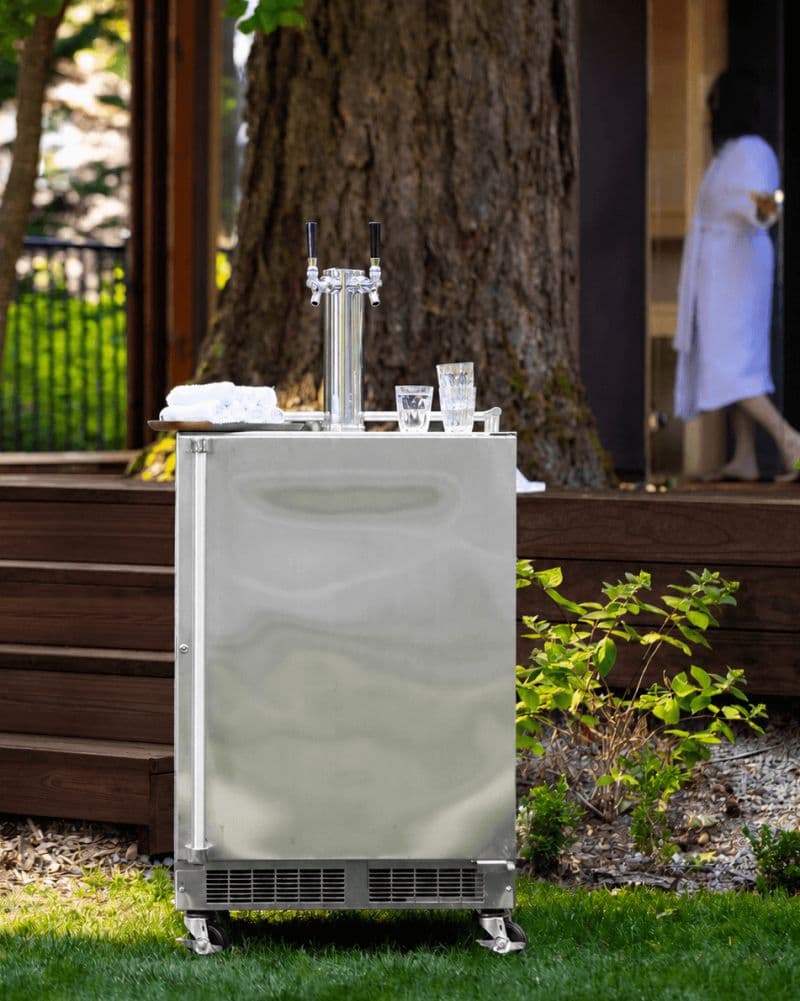 Outdoor kitchen with a Marvel outdoor-rated refrigerator + kegerator built into a stone island, at dusk with warm lantern lighting.
