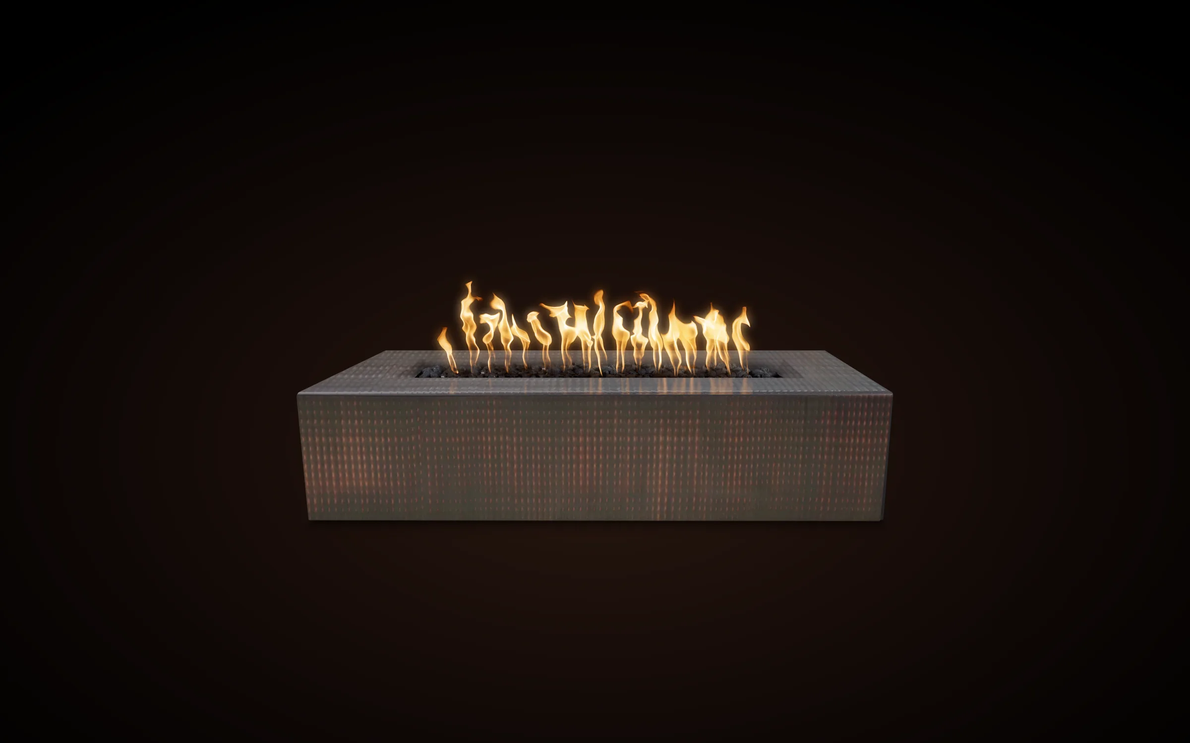 The Outdoor Plus Regal 60-inch rectangular fire pit in hammered copper with the natural-gas burner lit, flames rising from the lava-rock bed — official TOP product photography composed on a warm-dark editorial background.